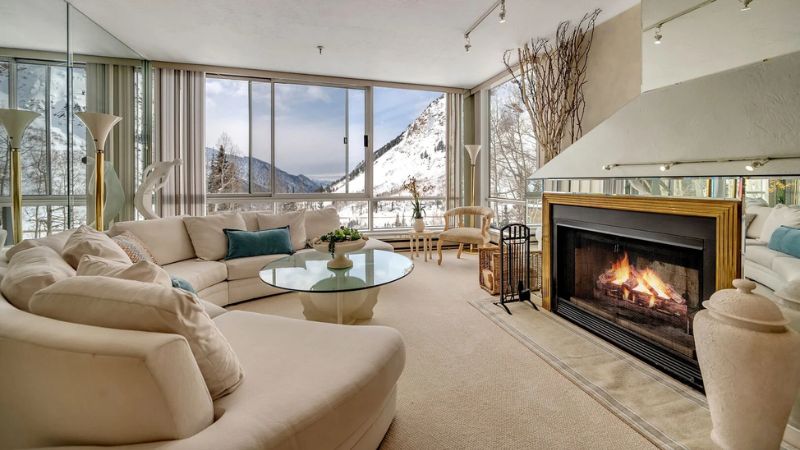 Living room with a fireplace and large windows overlooking snowy mountains.