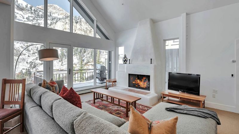 Cozy living room with a fireplace and mountain views through tall windows.