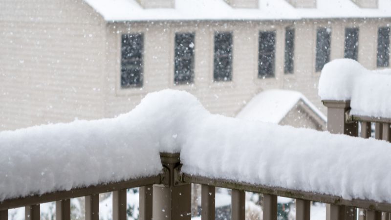 Snow piling up on a balcony railing during heavy snowfall.