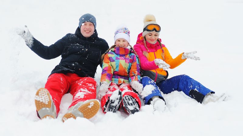 Family in colorful winter clothing sitting in the snow and playing together.