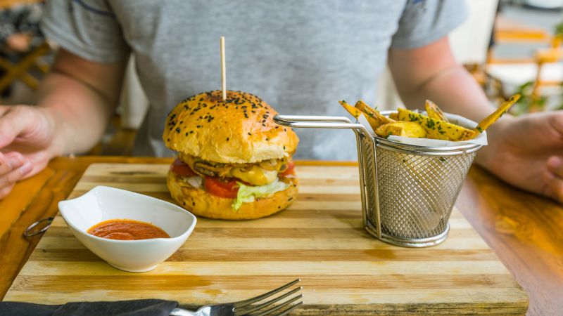 A burger with fries and dipping sauce served on a wooden board.