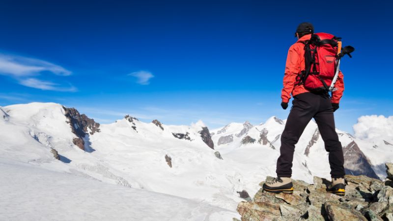 A man with a backpack standing on a snowy mountain peak, enjoying the view.