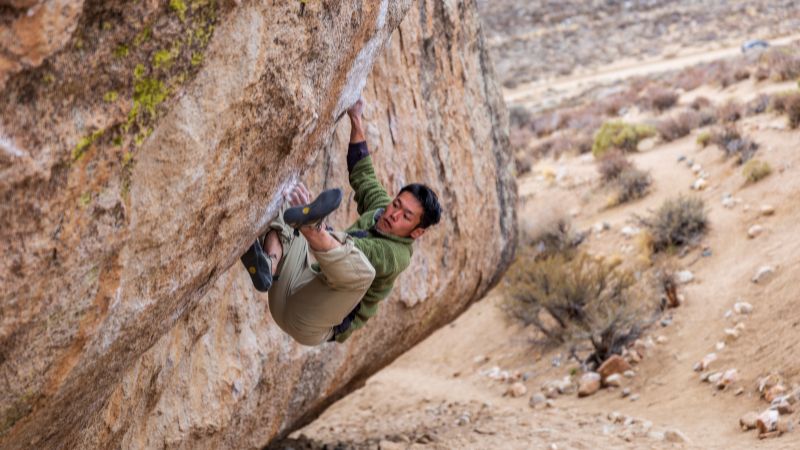 Man bouldering on an overhanging rock face in a desert landscape.