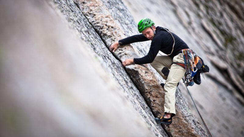 Rock climber ascending a vertical crack in a granite wall with gear.